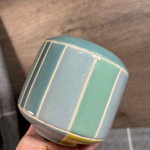 Op de afbeelding: Een keramische plantenpot met een gestreept ontwerp in tinten blauw, groen en geel.