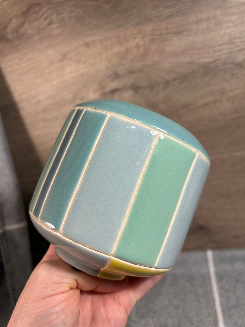 Op de afbeelding: Een keramische plantenpot met een gestreept ontwerp in tinten blauw, groen en geel.