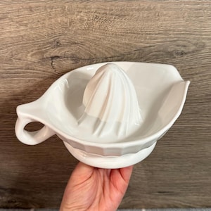 May include: White ceramic citrus juicer with a built-in reamer and a pouring spout. The juicer has a handle and a ridged cone for extracting juice. The design is simple and functional, ideal for making fresh juice at home.
