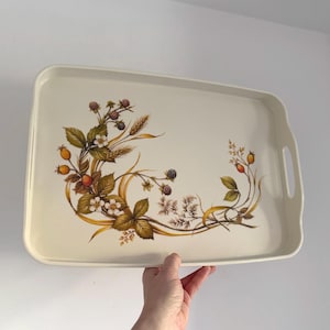 May include: Cream-coloured rectangular serving tray with a botanical design. The tray features an illustration of berries, wheat, and leaves in brown, green, and yellow. It has integrated handles for easy carrying.