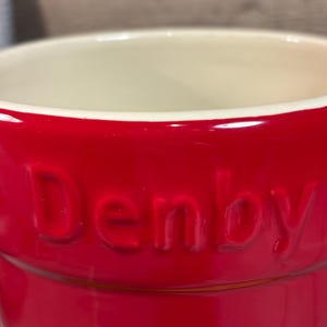 May include: A red ceramic utensil holder with the word "Denby" embossed on the side.