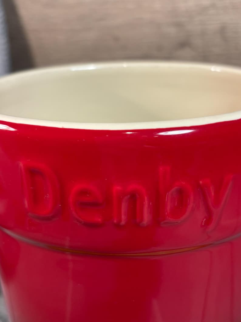May include: A red ceramic utensil holder with the word "Denby" embossed on the side.