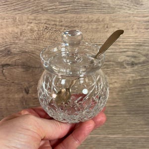 Puede incluir: Un tarro de vidrio transparente con tapa y una cucharita. El tarro tiene un diseño de vidrio cortado y es perfecto para guardar azúcar, miel u otros artículos pequeños.