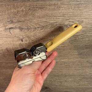 May include: A silver knife sharpener with a beige plastic handle. The sharpener has two sets of ceramic sharpening slots.