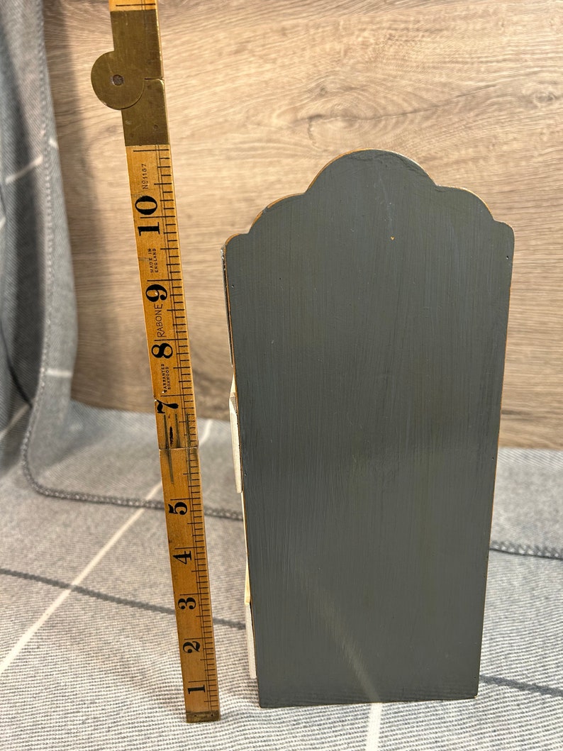 May include: A small wooden storage box with four drawers. The box is painted grey and white and has a decorative top. The box is about 15 cm tall.