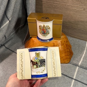 May include: Two fine bone china beakers. One is a Golden Jubilee commemorative piece from 1952-2002, featuring a royal crest. The other beaker celebrates Ringtons Centenary, 1907-2007, with a horse-drawn carriage design. Both are in their original boxes.