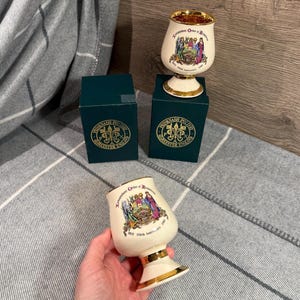 May include: A cream-coloured goblet with gold trim, displaying a colourful illustration and text. Two green boxes with gold lettering and a logo are also visible. The goblet is labelled "Independent Order of Rechabites" and "150th Anniversary".