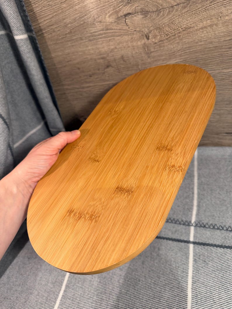 May include: An oval-shaped wooden serving tray with a smooth, light brown finish and visible natural wood grain patterns. The tray features rounded edges and a flat surface, showcasing the organic texture and warm tones of the wood material.