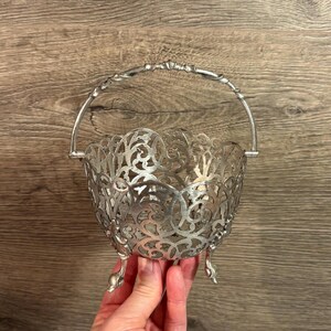 May include: An antique silver basket with an intricate openwork design. The basket has a handle and three small feet. The openwork pattern features floral and scroll motifs, creating a delicate and decorative appearance.