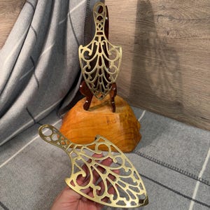 Può includere: Due porta tostapane antichi in ottone a forma di ovale appuntito. I porta tostapane hanno un design decorativo e intricato con dettagli tagliati.