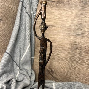 Escultura antigua de bronce africano, alta y delgada, hecha a mano, que representa a una mujer tribal cargando a un bebé y una vasija de agua sobre su cabeza.