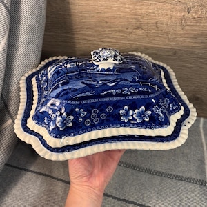 Puede incluir: Plato de servir de porcelana azul y blanco con tapa. El plato tiene un borde festoneado y un diseño floral. La tapa tiene un pomo en la parte superior.