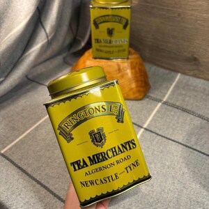 以下が含まれることがあります： 黒い文字で「RINGTONS LTD TEA MERCHANTS ALGERNON ROAD NEWCASTLE UPON TYNE」と書かれた黄色の金属製の茶缶。