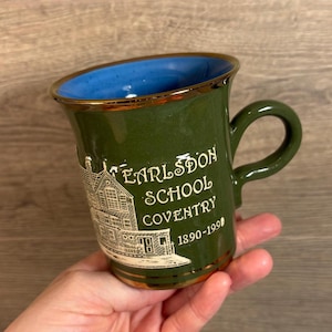 May include: A green ceramic mug with a gold rim and a blue interior. It features a white image of a building with the text "Earlsdon School Coventry 1890-1990".