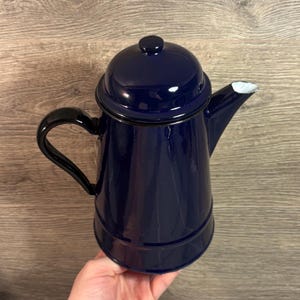 May include: A navy blue enamel coffee pot with a black handle and lid. The spout has a white interior. The pot is a classic design, suitable for brewing coffee or tea. The pot is approximately 20 cm tall.