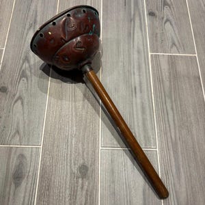 Op de afbeelding: Een vintage koperen en houten plunjer met een houten handvat. Het koperen deel heeft een decoratief ontwerp en gaten voor drainage.