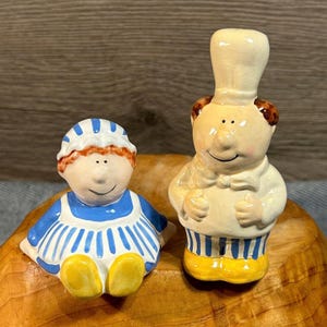 Chapéu de gravata borboleta vintage feliz, chef e sua alegre dama em uniformes de listras azuis pastel combinando e sapatos amarelos, saleiros e pimenteiros