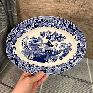 Può includere: Un piatto da portata ovale bianco con un motivo di salice blu e bianco. Il motivo presenta una pagoda, un ponte e alberi.