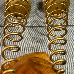 Peut inclure: Deux bougeoirs en m&eacute;tal dor&eacute; avec un design en spirale. Les bougeoirs sont pos&eacute;s sur une surface en bois.