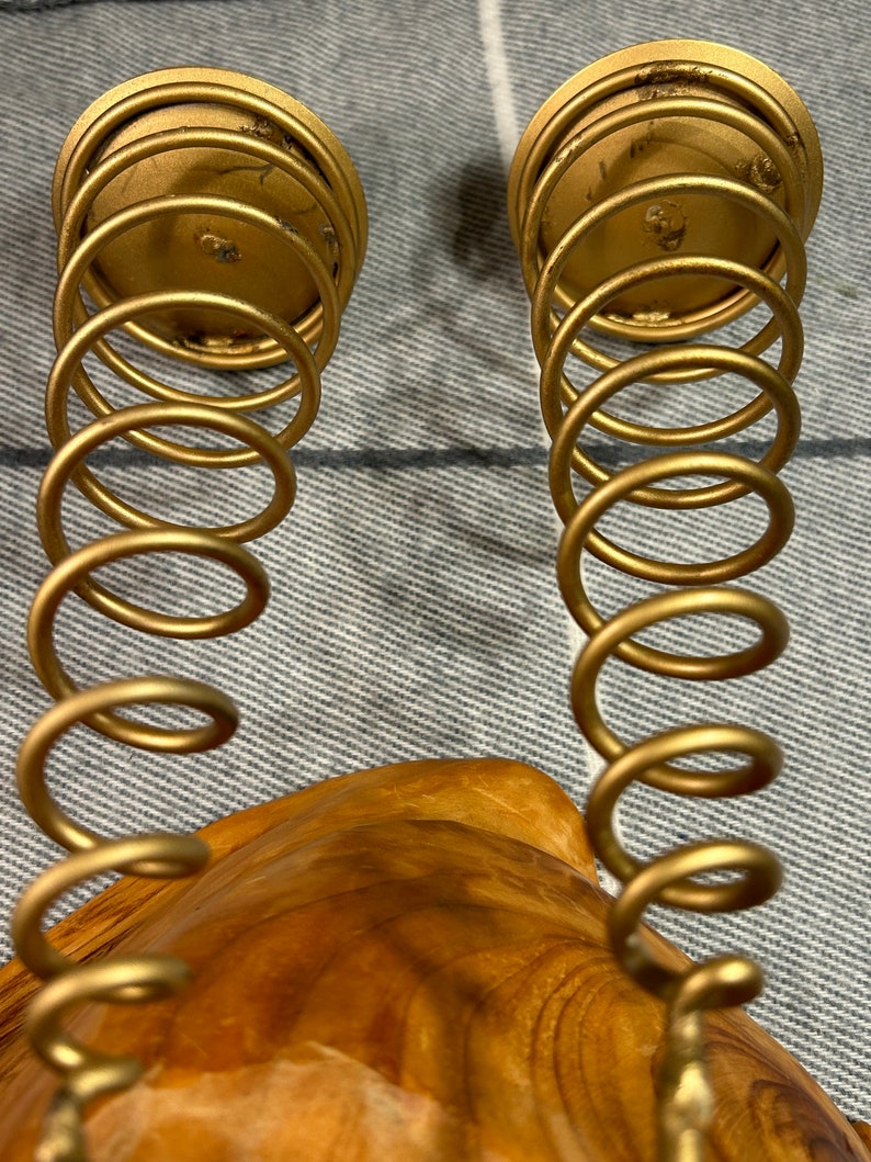Peut inclure: Deux bougeoirs en m&eacute;tal dor&eacute; avec un design en spirale. Les bougeoirs sont pos&eacute;s sur une surface en bois.