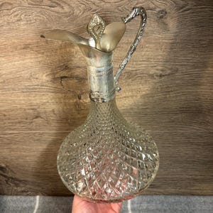 May include: A clear glass decanter with a diamond pattern and a silver-tone lid and handle.