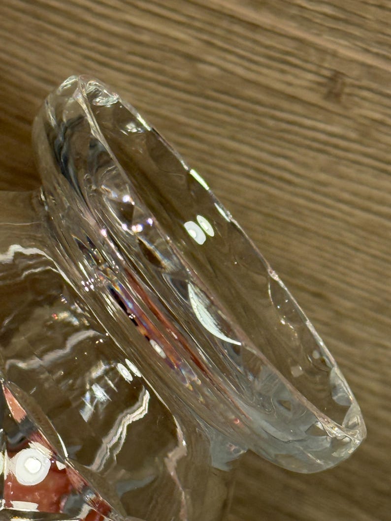 Op de afbeelding: Een helder glazen object met een brede, gebogen rand. Het glas heeft een getextureerd oppervlak en reflecteert licht, waardoor highlights en schaduwen ontstaan. Het object lijkt een decoratief stuk of een deel van een groter vat te zijn.