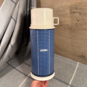 May include: A vintage Thermos flask with a blue patterned design. The flask has a white lid and base. The blue body features a pattern of small, light blue circles. The word "THERMOS" is printed on the front. The lid has a handle.