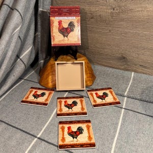 May include: A set of four country-themed coasters with a matching box. Each coaster and the box feature a rooster illustration in red, black, and brown. The coasters are square and have a decorative border.