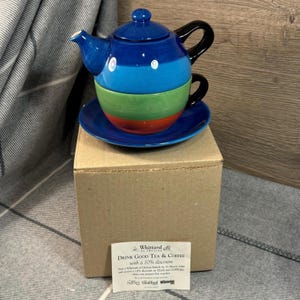 Puede incluir: Un juego de tetera y taza de cerámica a rayas azules y verdes con un platillo a juego. El juego está sobre una caja marrón con una etiqueta de Whittard of Chelsea que dice "Drink Good Tea & Coffee with a 10% discount".
