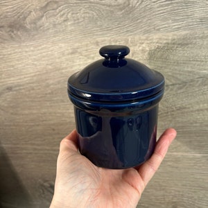 Puede incluir: Un tarro de cerámica azul oscuro con tapa. El tarro tiene un acabado brillante y es de tamaño pequeño.
