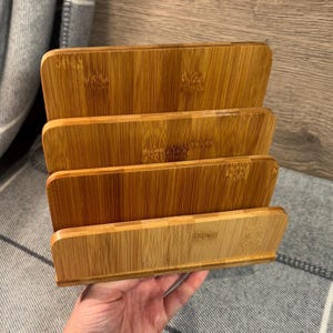 May include: A bamboo desk organiser with four tiered slots. The organiser is made of light brown bamboo and has a natural wood grain finish. The slots are designed to hold papers, mail, or other office supplies.