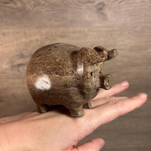 Könnte beinhalten: Eine kleine, braune, geschnitzte Schweinefigur mit einer strukturierten Oberfläche. Das Schwein hat eine leicht nach oben gerichtete Schnauze und kleine, runde Ohren.