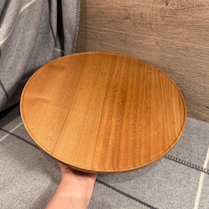 May include: A circular wooden serving tray with a smooth, light brown finish and visible natural wood grain patterns. The tray features a slightly raised edge around the perimeter, providing a clean, flat surface for various household items.