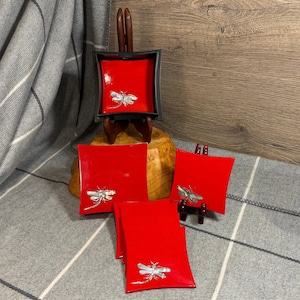 May include: Set of four red lacquer square trays with silver dragonfly accents. The trays are displayed on a wooden stand.