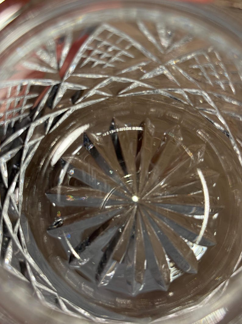 Op de afbeelding: Close-up van een helder glas met ingewikkelde geslepen kristallen patronen. Het ontwerp heeft geometrische vormen en radiale lijnen die uit het midden komen en een sterrenburst-effect cre&euml;ren. Het glas is waarschijnlijk voor dranken.