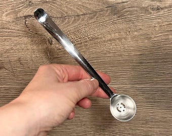 May include: A silver spoon with a long handle and a round bowl with holes. The bowl has a decorative pattern.