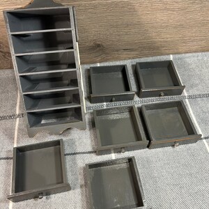 May include: A black wooden organiser with seven shelves and five drawers. The organiser is made of wood and has a distressed finish.
