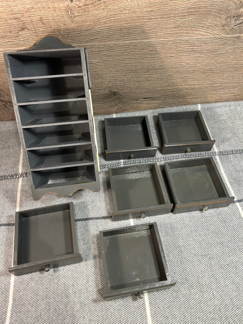 May include: A black wooden organiser with seven shelves and five drawers. The organiser is made of wood and has a distressed finish.