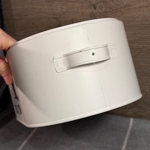 May include: A cylindrical white metal storage container featuring a horizontal handle attached to the side. The container has a smooth, solid white finish with a visible vertical seam running down the side and a small central hole in the handle.