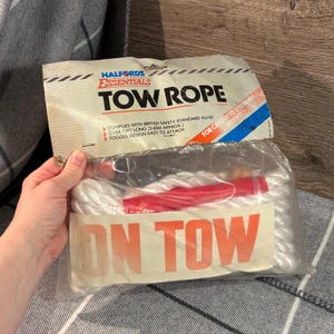 Könnte beinhalten: Ein weißes Abschleppseil in einer transparenten Kunststoffverpackung. Auf der Verpackung steht "HALFORDS ESSENTIALS TOW ROPE" und "ON TOW" in Orange. Das Seil ist über 3,65 m lang und für Autos bis zu 2 Tonnen geeignet.