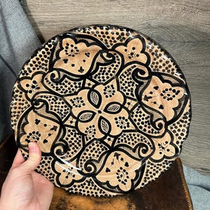 Puede incluir: Un plato grande y redondo de cerámica con un diseño geométrico en blanco y negro. El plato tiene un borde festoneado y está decorado con un patrón repetitivo de puntos y espirales.