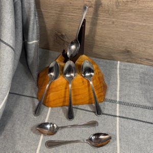 Könnte beinhalten: Sechs silberne Löffel mit einem perlenbesetzten Rand. Die Löffel sind in einem Holzhalter angeordnet.