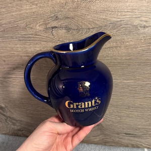 May include: A dark blue ceramic jug with a gold rim and handle. The jug features the "Grant's Scotch Whisky" logo in gold lettering. The jug is a classic design, suitable for serving beverages.