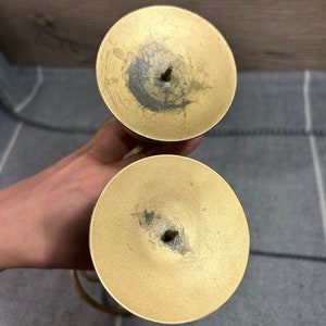 Peut inclure: Un ensemble de deux bougeoirs en m&eacute;tal dor&eacute; au design simple. Chaque bougeoir a une base ronde et un sommet circulaire avec un petit trou au centre pour une bougie.