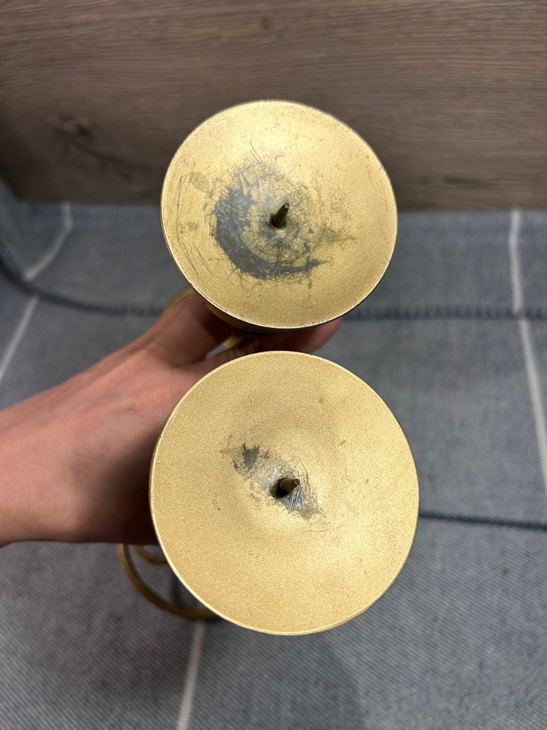 Peut inclure: Un ensemble de deux bougeoirs en m&eacute;tal dor&eacute; au design simple. Chaque bougeoir a une base ronde et un sommet circulaire avec un petit trou au centre pour une bougie.