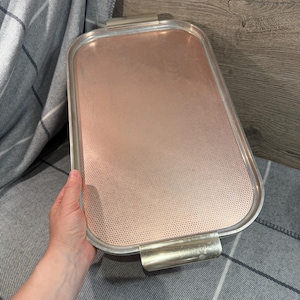 May include: A rectangular serving tray with a copper-coloured interior and a silver-coloured metal frame. The tray has two handles and a perforated surface. The tray is approximately 35 cm long and 23 cm wide.