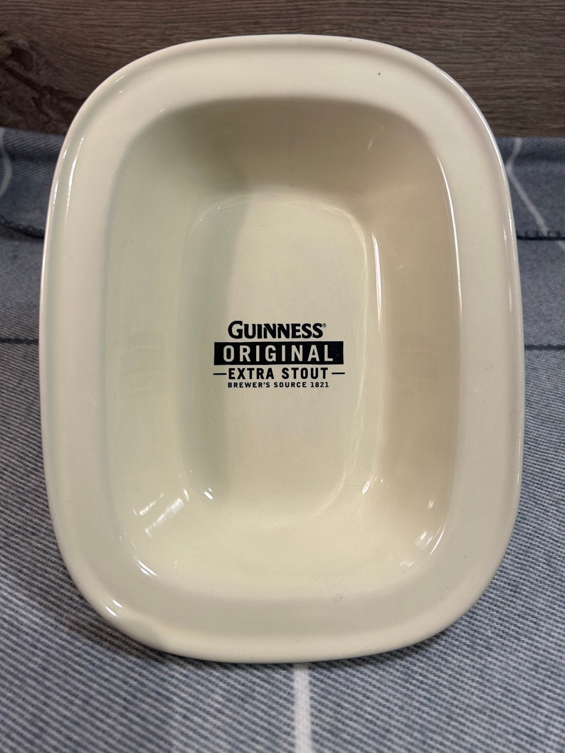 May include: Cream-colored, rectangular serving dish with rounded corners. The dish features the Guinness Original Extra Stout logo in black. The text reads "Brewer's Source 1821".