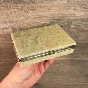 May include: A rectangular, light green, decorative box with a silver trim. The box is made of alabaster and has a swirling pattern.
