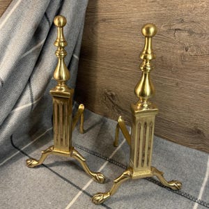 Pode incluir: Um par de suportes de lareira de latão antigo com detalhes ornamentados e pés em forma de pata.