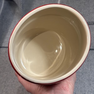 May include: A red ceramic container with a white interior. The container is empty and appears to be made of a durable material.